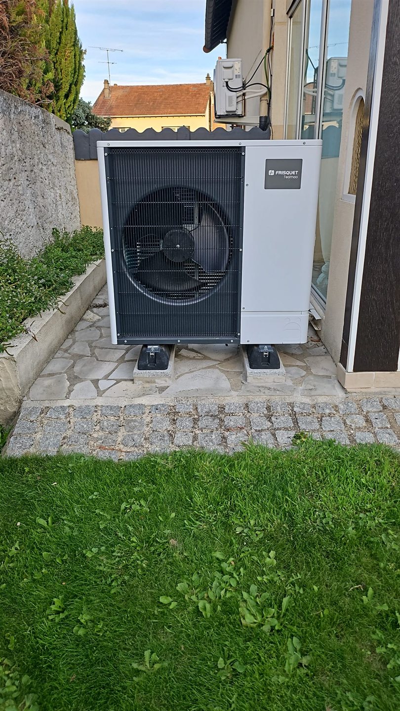 Groupe extérieur de pompe à chaleur Frisquet installé sur plots, devant une pelouse